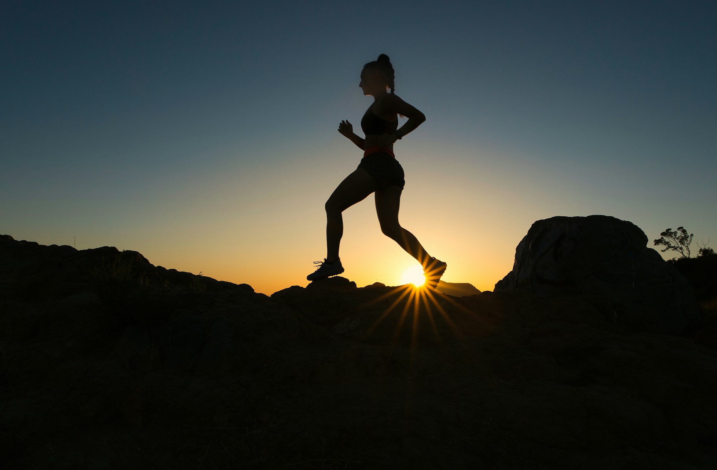 Silhouette of woman running across rocks at sunrise